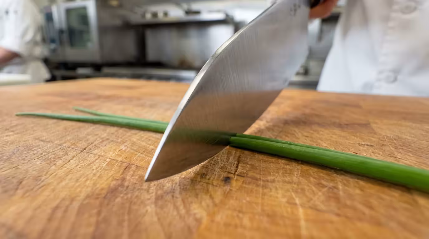 A macro low-angle photo of a sharp knife blade touching an end-grain wood cutting board.