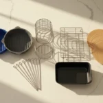 An overhead view of various air fryer accessories like silicone liners, metal racks, and a small baking pan, neatly displayed on a light kitchen counter with warm morning light.
