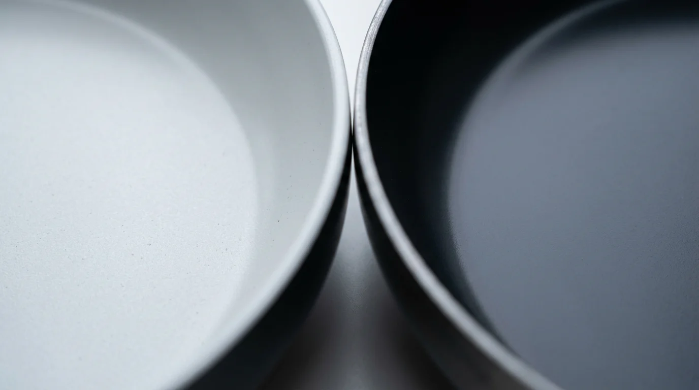 Close-up macro photo comparing the surface of a light gray ceramic pan and a dark PTFE pan.